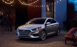 A silver 2022 Hyundai Accent parked in front of a building with lights hanging around the top. | Hyundai dealer in Fort Smith, AR.
