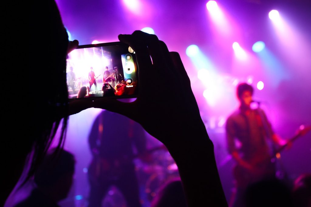 A girl in the crowd recording a band performing on stage in front of her. | Things to do near Fort Smith, AR | Crain Hyundai of Fort Smith